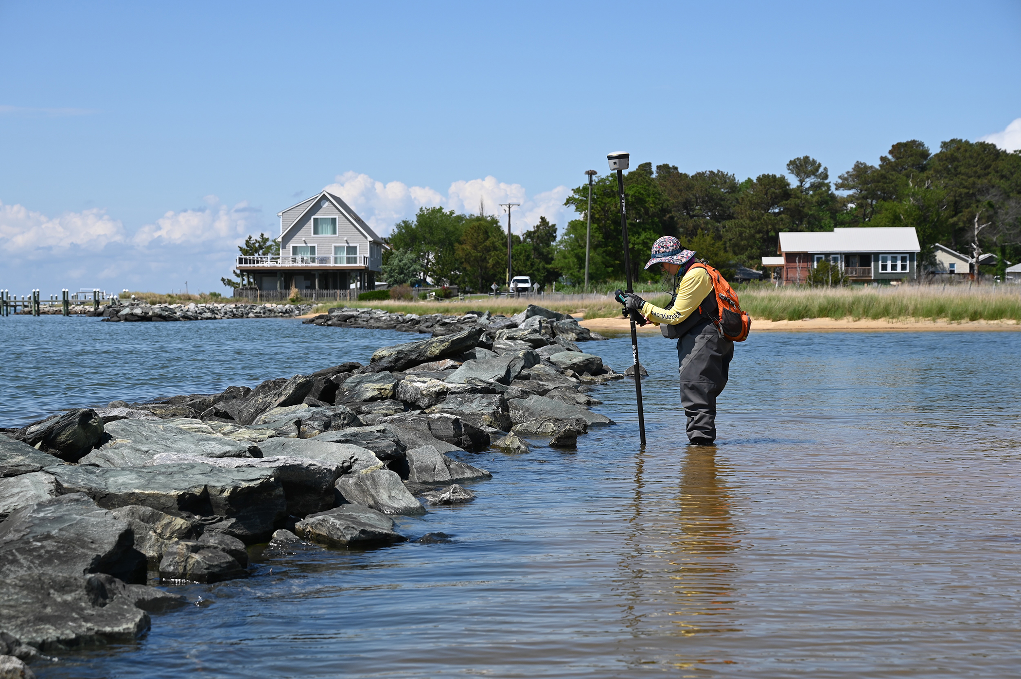 person in waders measuring depth of water they are standing in, in front wall of rocks in the water.